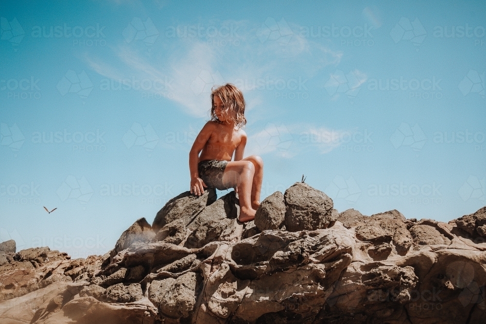 Boy sitting on rocks looking at a butterfly - Australian Stock Image