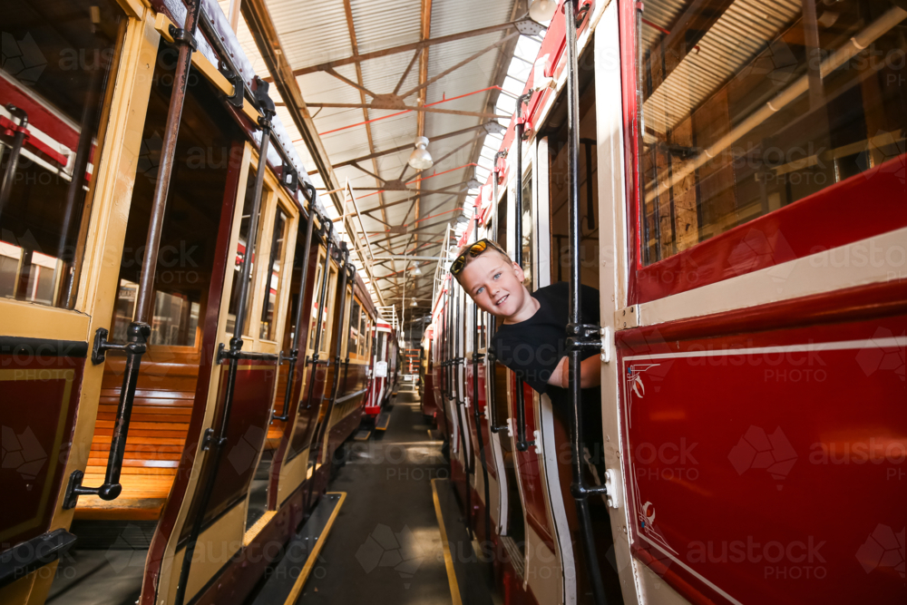Boy smiling on vintage tram, looking out from window in historic depot - Australian Stock Image
