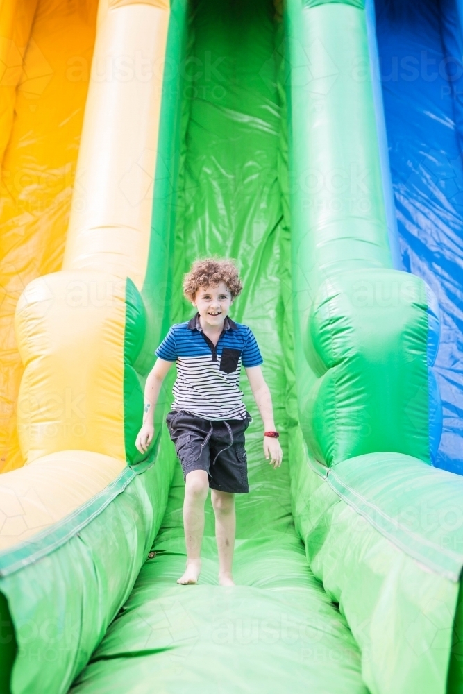 Boy smiling running on blow up slide at local show - Australian Stock Image