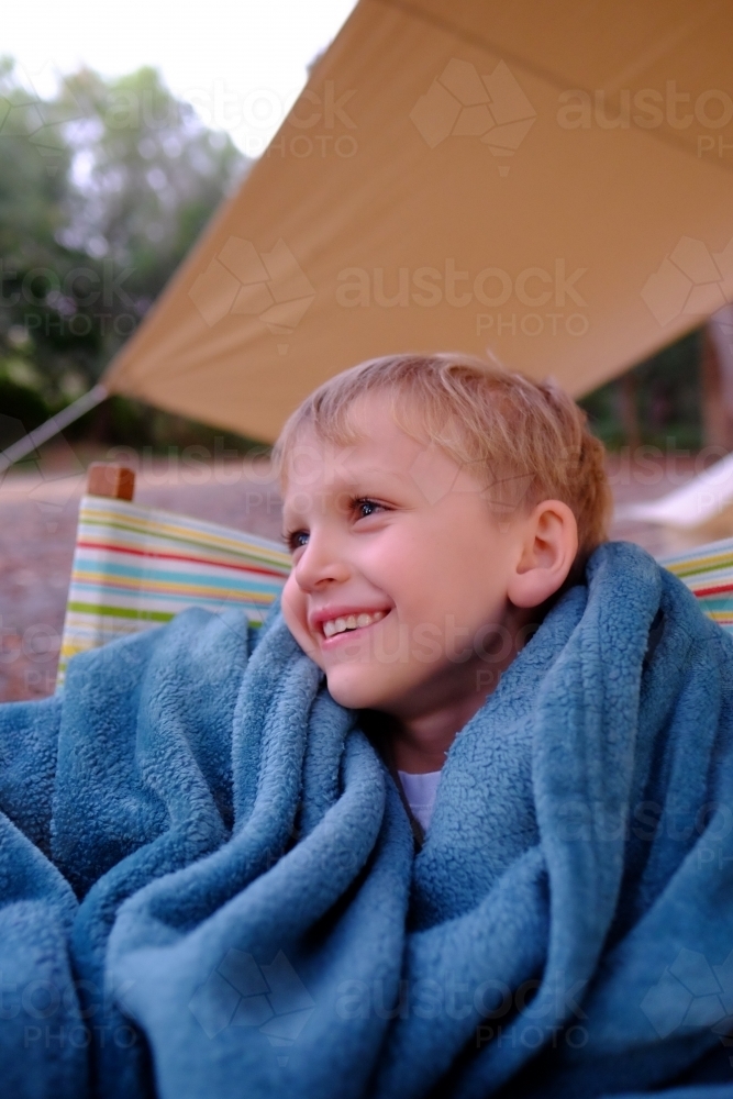 Boy smiling, sitting outside tent in camping chair - Australian Stock Image