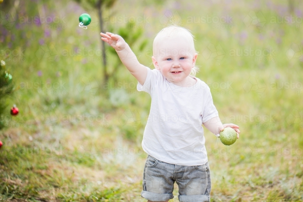 Boy smiling throwing Christmas bauble outdoors - Australian Stock Image