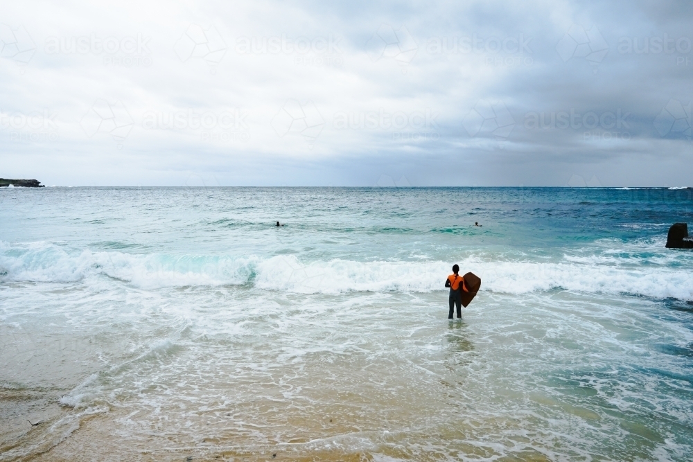 Boy standing at beach with bodyboard - Australian Stock Image
