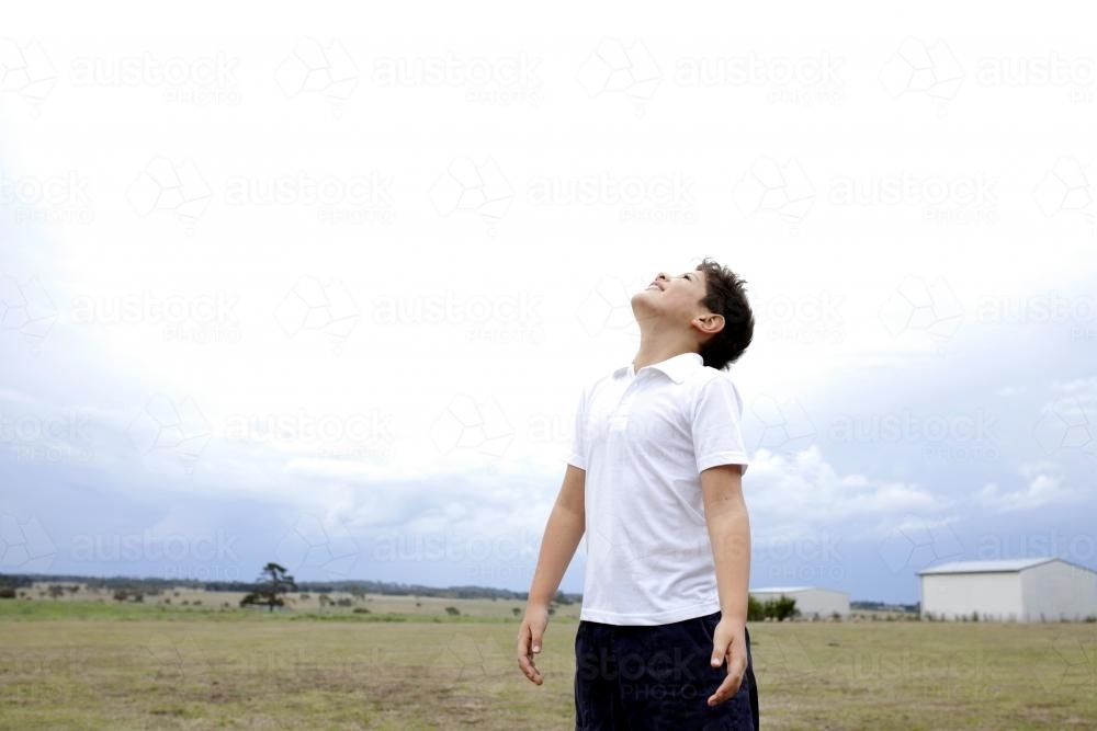 Boy standing in open field looking up at sky - Australian Stock Image