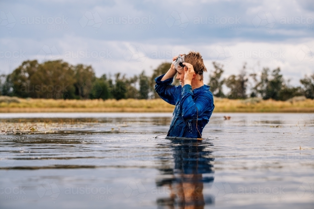 Boy standing in water with goggles looking into the distance - Australian Stock Image