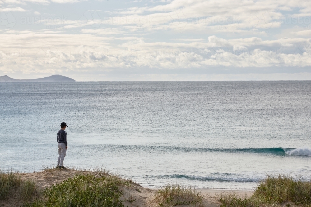Boy standing on sand dune looking out to sea - Australian Stock Image