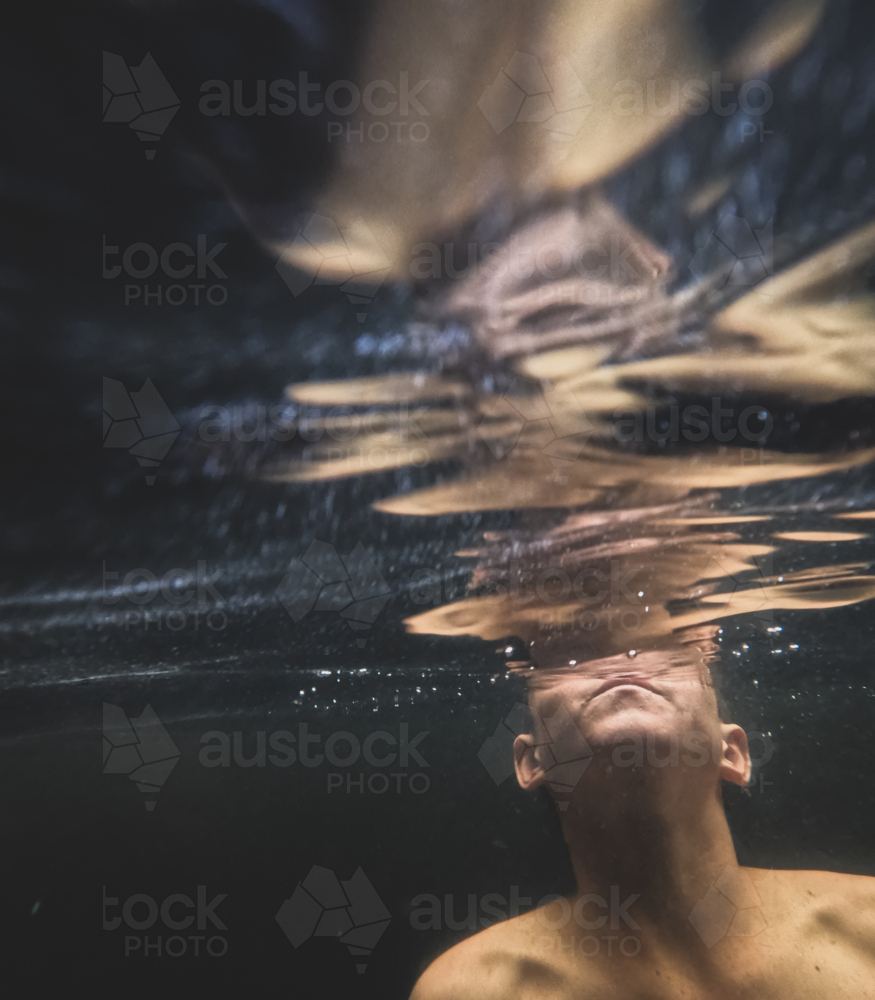 Boy submerged under clear water with shoulders and lower face visible blowing bubbles to surface - Australian Stock Image