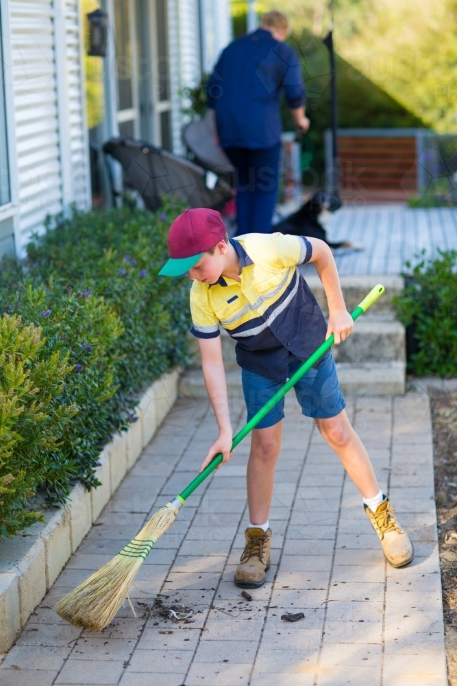 Boy sweeping path with raw broom - Australian Stock Image