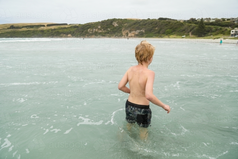 Boy swimming at the beach on cold winter day - Australian Stock Image