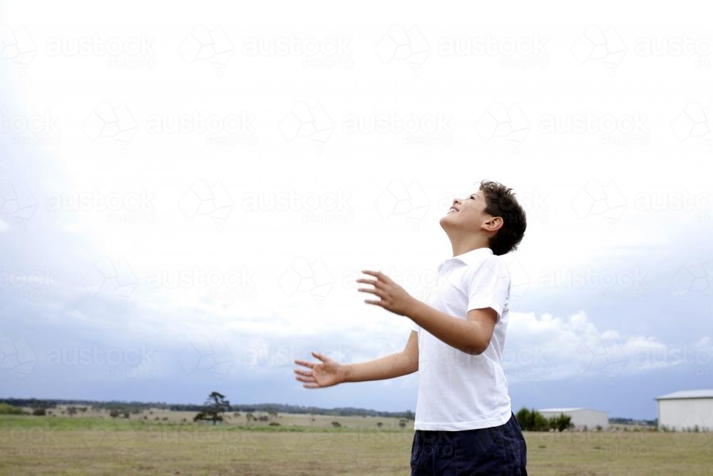 Boy throwing ball up into air, looking up at sky - Australian Stock Image