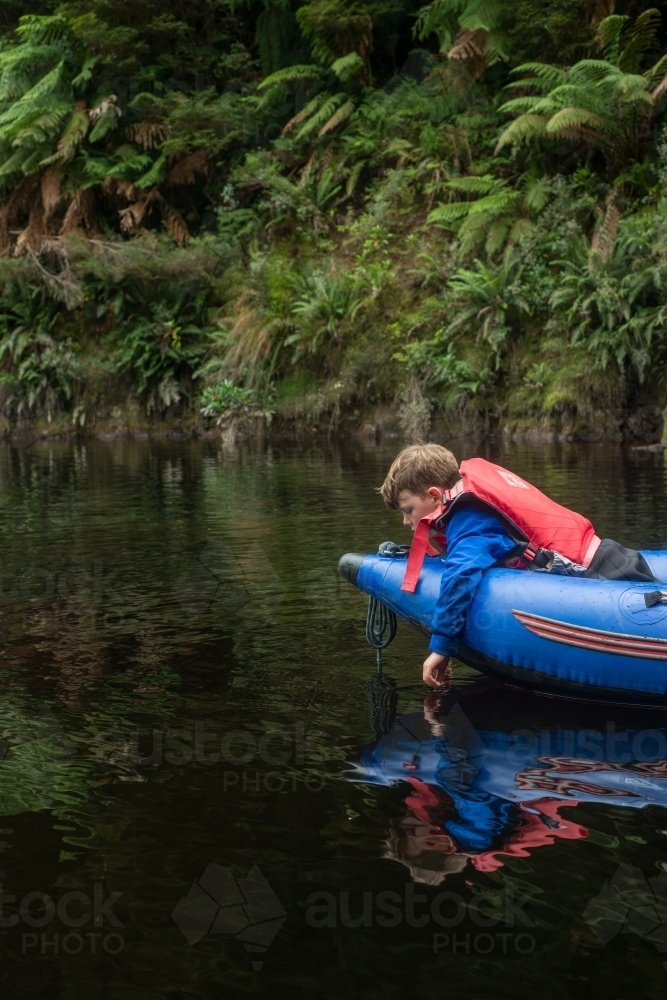 Boy trailing his hand in river water from a kayak - Australian Stock Image