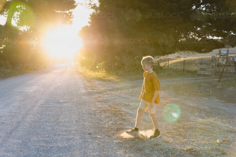 Boy walking on quiet country road near farm - Australian Stock Image