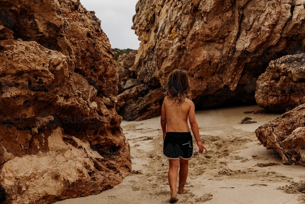 Boy walking through gap in rocks on beach - Australian Stock Image