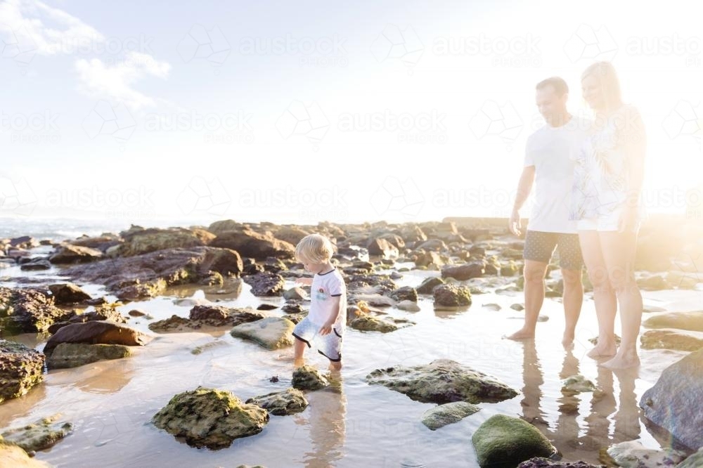 Boy walking through rockpool while parents watch on - Australian Stock Image