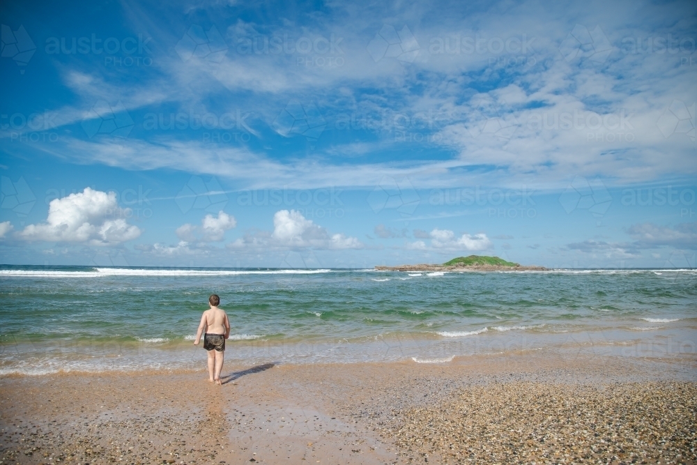 Boy walking towards the water on the beach at Coffs Harbour - Australian Stock Image