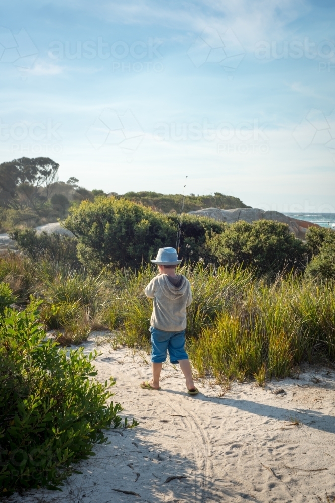 Boy walking with fishing rod on path to beach - Australian Stock Image