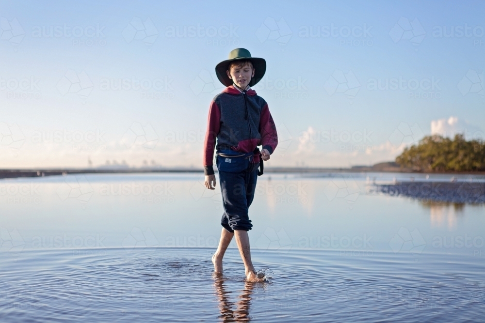Boy walks on the beach at lowtide in winter barefoot - Australian Stock Image
