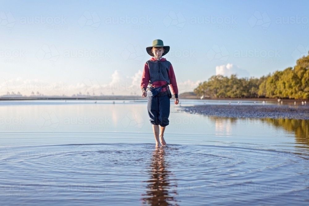 Boy walks on the beach at lowtide in winter barefoot - Australian Stock Image