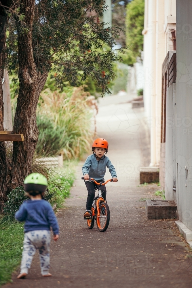 Boy wearing an orange helmet riding his bike on the footpath - Australian Stock Image
