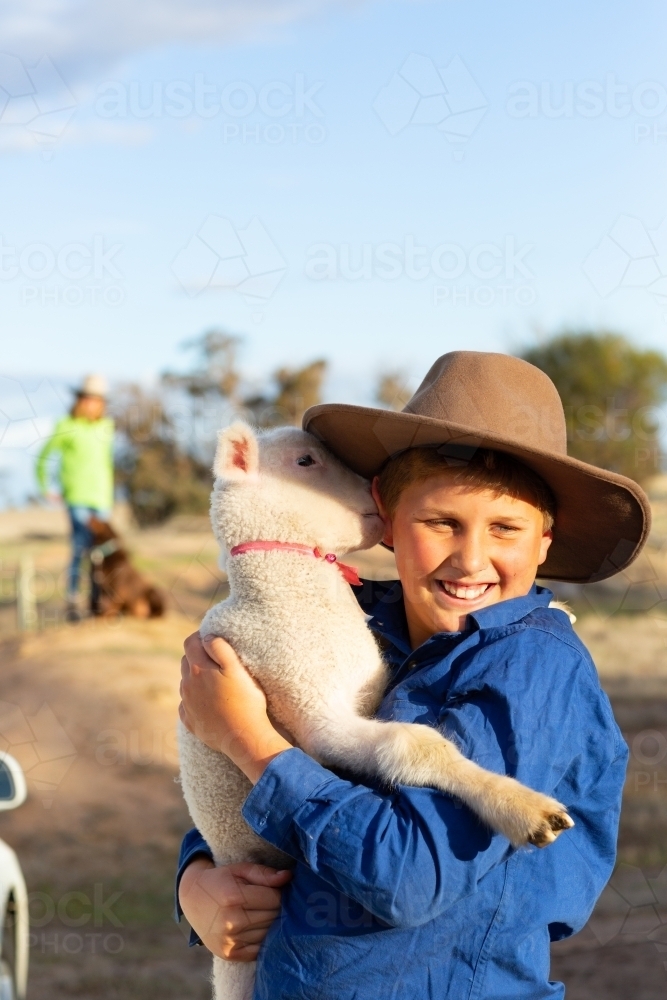 Boy wearing hat holding his pet lamb - Australian Stock Image