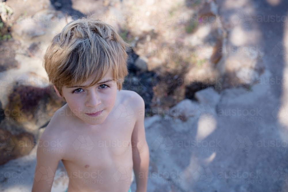 Boy wearing no shirt, looking up at camera at the beach - Australian Stock Image