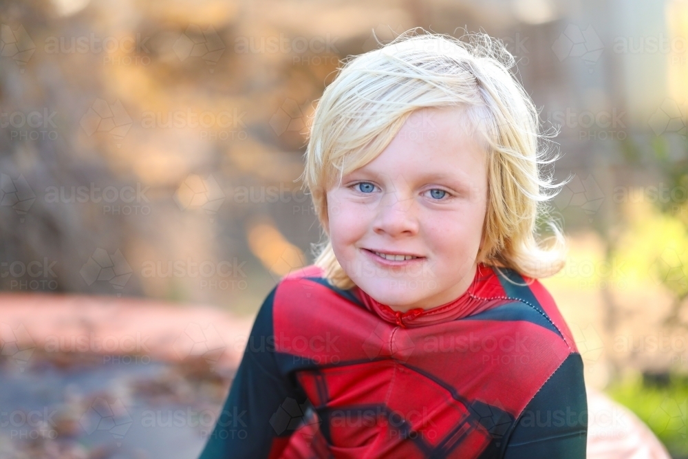 Image of Boy wearing red superhero suit sitting on trampoline covered