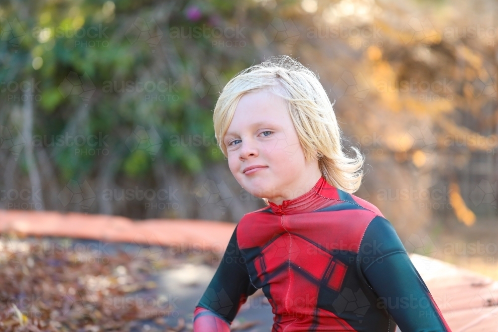 Image of Boy wearing red superhero suit sitting on trampoline covered