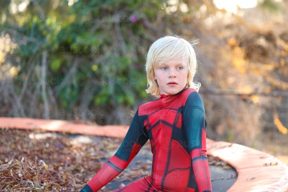 Image of Boy wearing red superhero suit sitting on trampoline covered