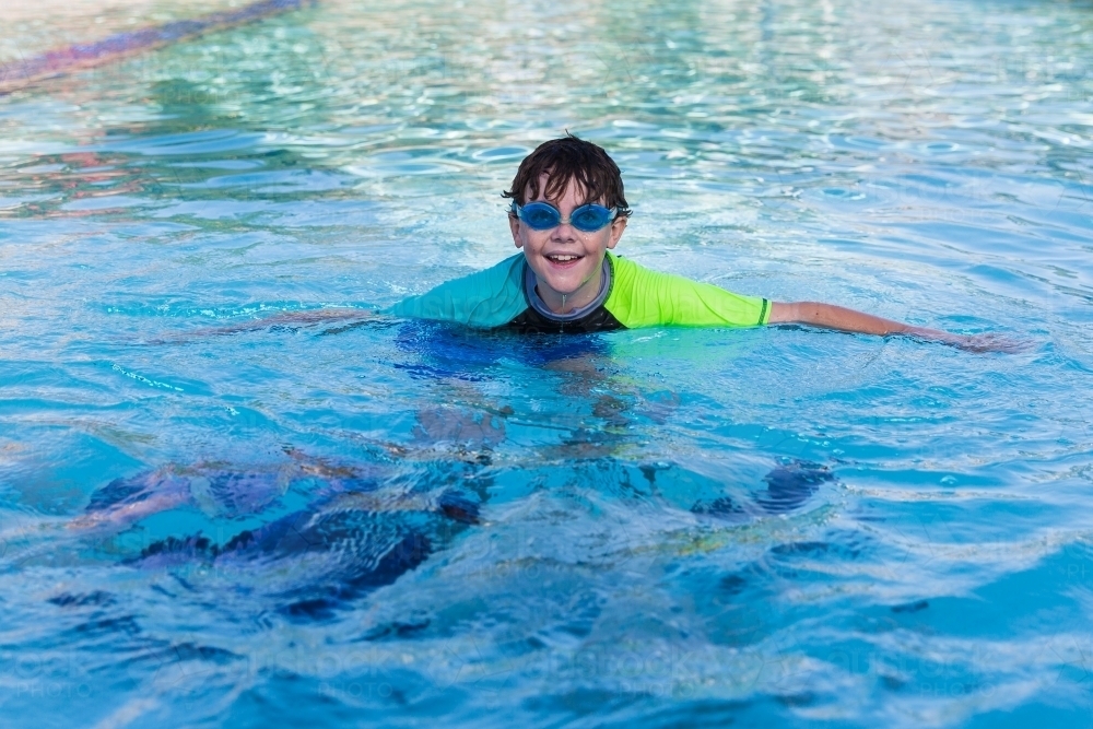 Boy wearing swimmers and goggles happy in pool - Australian Stock Image