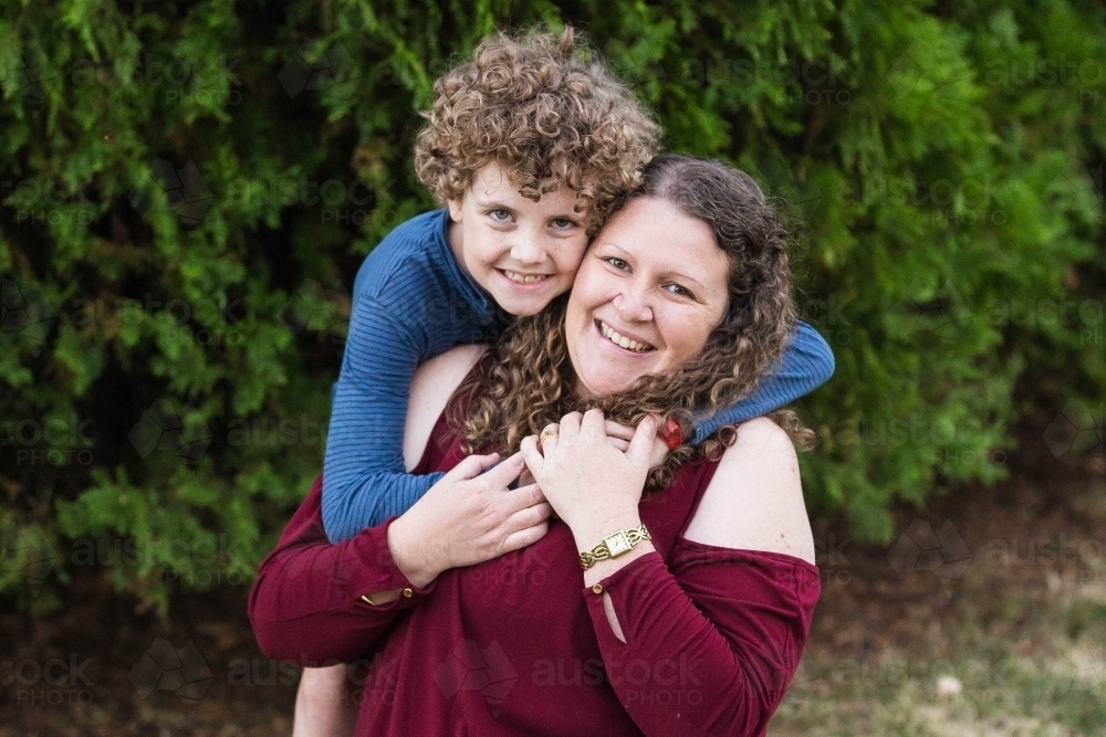 Boy with arms around mother sitting outside - Australian Stock Image