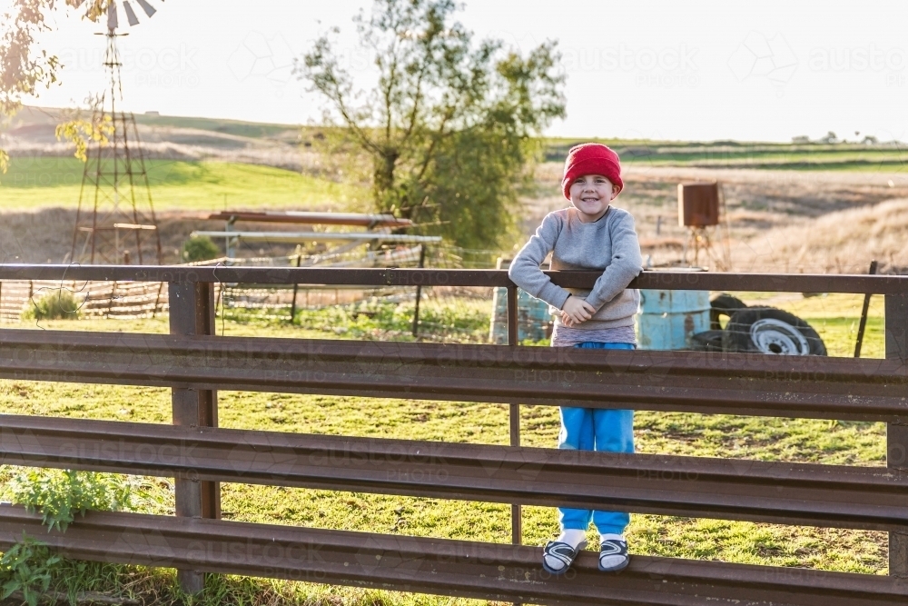 Image of Boy with beanie standing on fence of sheep yards - Austockphoto