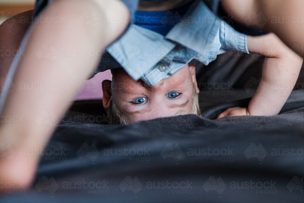 Boy with blue eyes up-side down on bed - Australian Stock Image