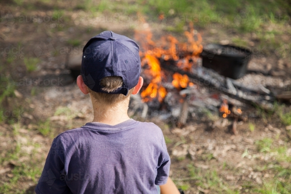 Boy with cap sitting around campfire - Australian Stock Image