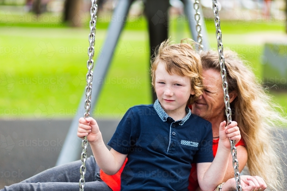 boy with carer on park swing equipment together - Australian Stock Image