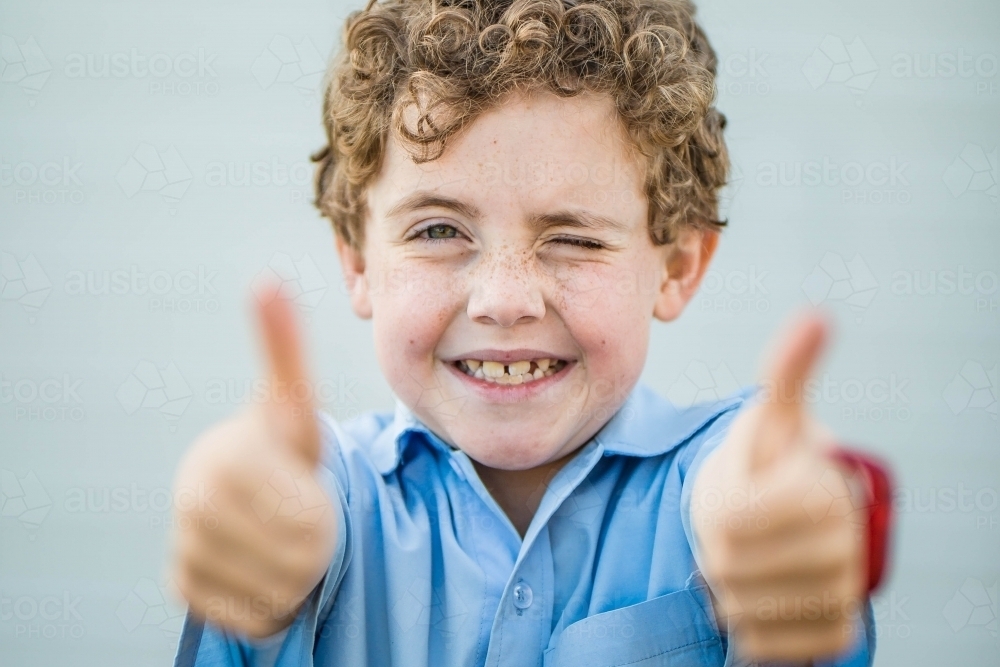 Boy with curly hair winking and smiling while giving thumbs up - Australian Stock Image
