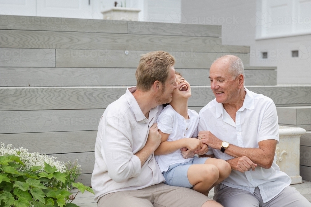 Boy with father and grandfather sitting on outdoor stairs - Australian Stock Image