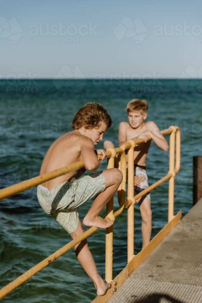 Boys climbing on Jetty by the sea - Australian Stock Image