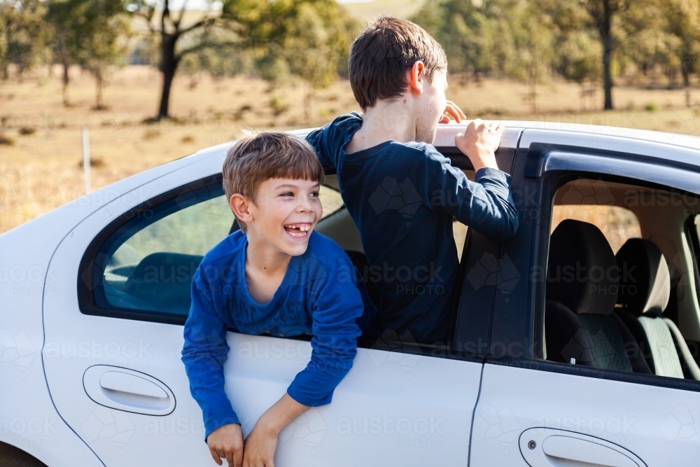 Boys climbing out of car window while waiting - Australian Stock Image