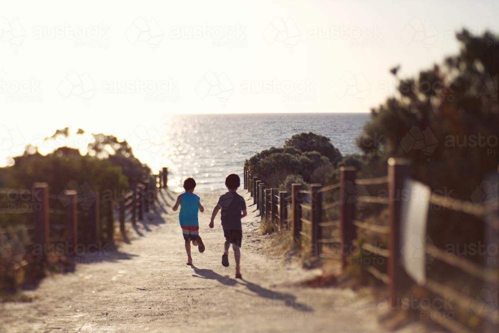 Boys running on sand to the beach - Australian Stock Image