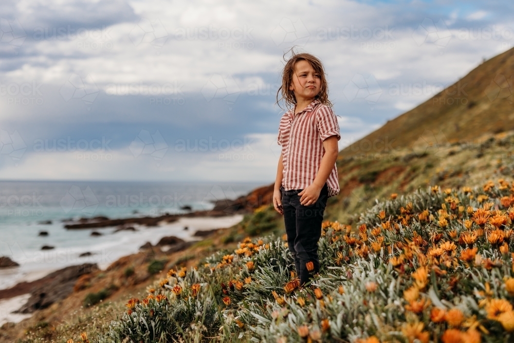 Boys standing on hill of flowers next to the ocean and rocks - Australian Stock Image