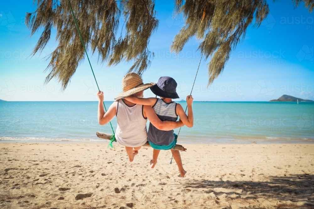 Boys swinging on log swing at Dingo Beach, near Airlie Beach in the Whitsundays, Queensland - Australian Stock Image