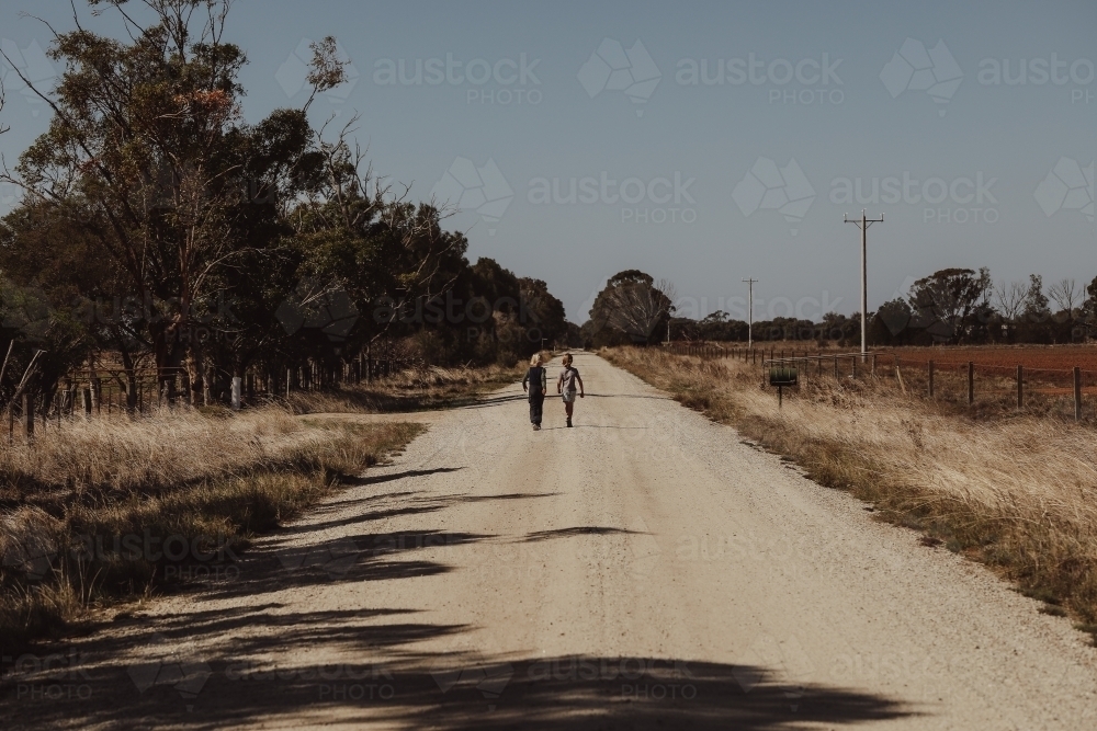 Boys walking along remote country road surrounded by fields - Australian Stock Image