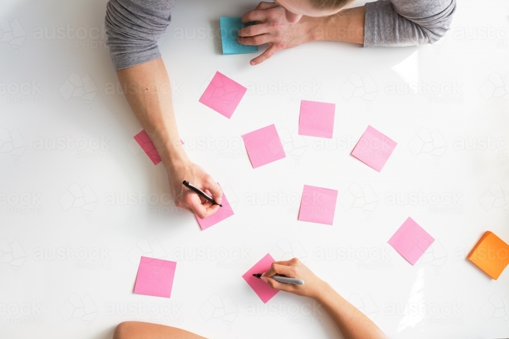 Brainstorming ideas on blank pink notes from overhead - Australian Stock Image