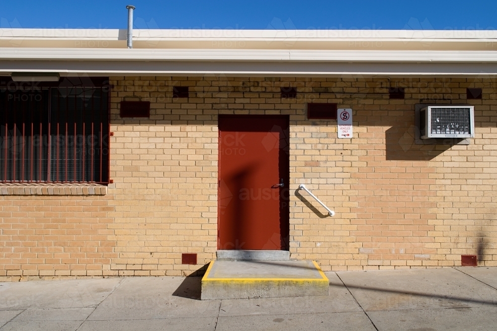 Brick building with a red door, yellow entry and under a blue sky - Australian Stock Image