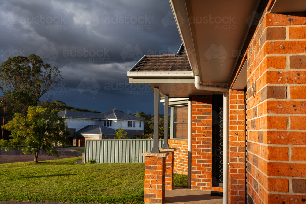 Brick duplex in sunset light with incoming storm clouds in sky - Australian Stock Image
