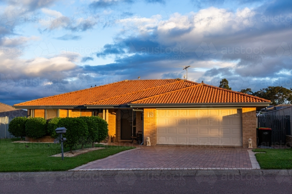 brick house with neat front lawn and double garage at sunset - Australian Stock Image