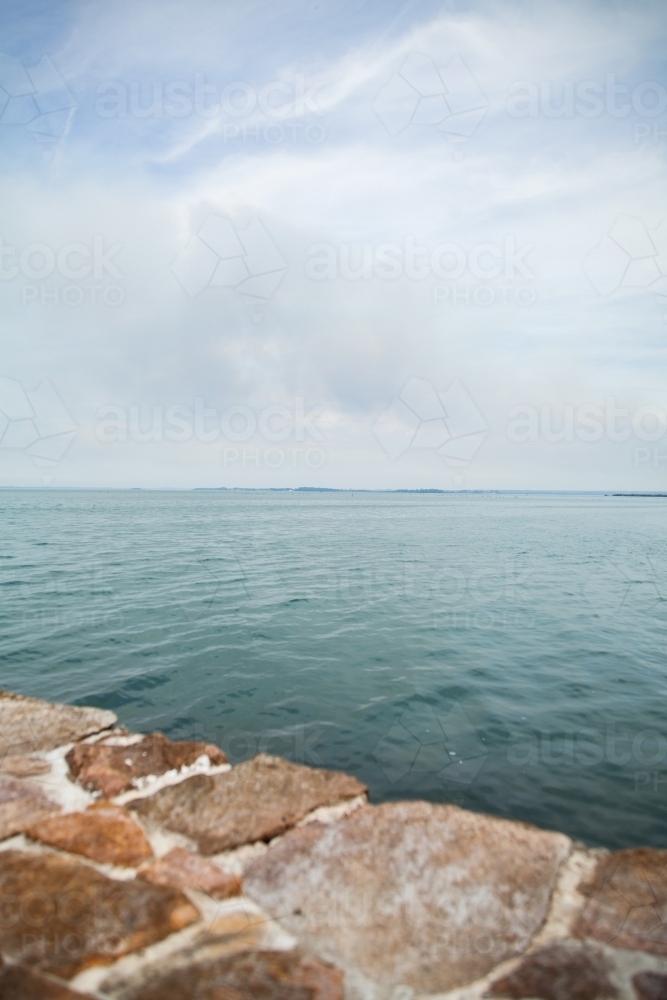Brick wall in foreground with bay leading to ocean behind - Australian Stock Image