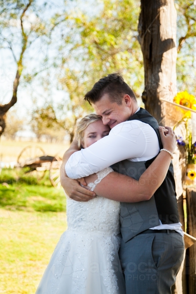 Bride and groom hug at outdoor country style ceremony - Australian Stock Image