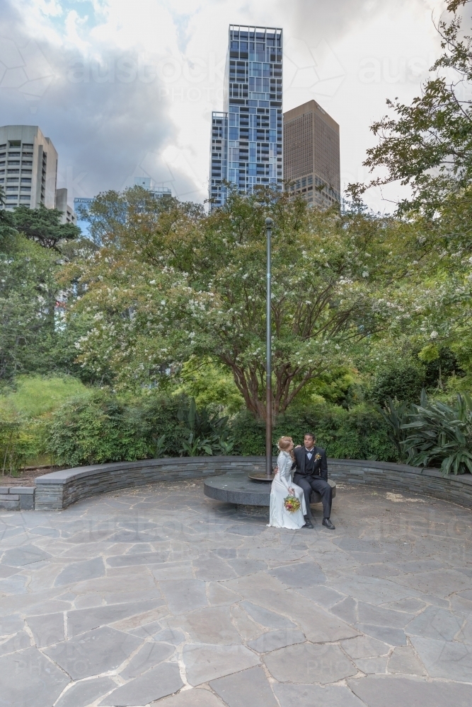 Bride and groom sitting together in city park - Australian Stock Image