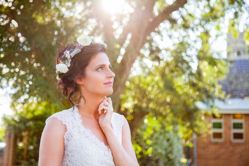 Bride looking away with dreamy expression in golden light flare - Australian Stock Image