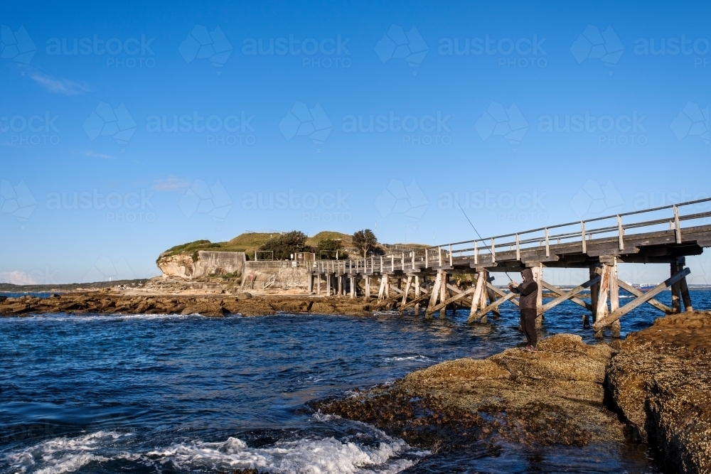 Bridge to Bare Island and rock fisherman - Australian Stock Image